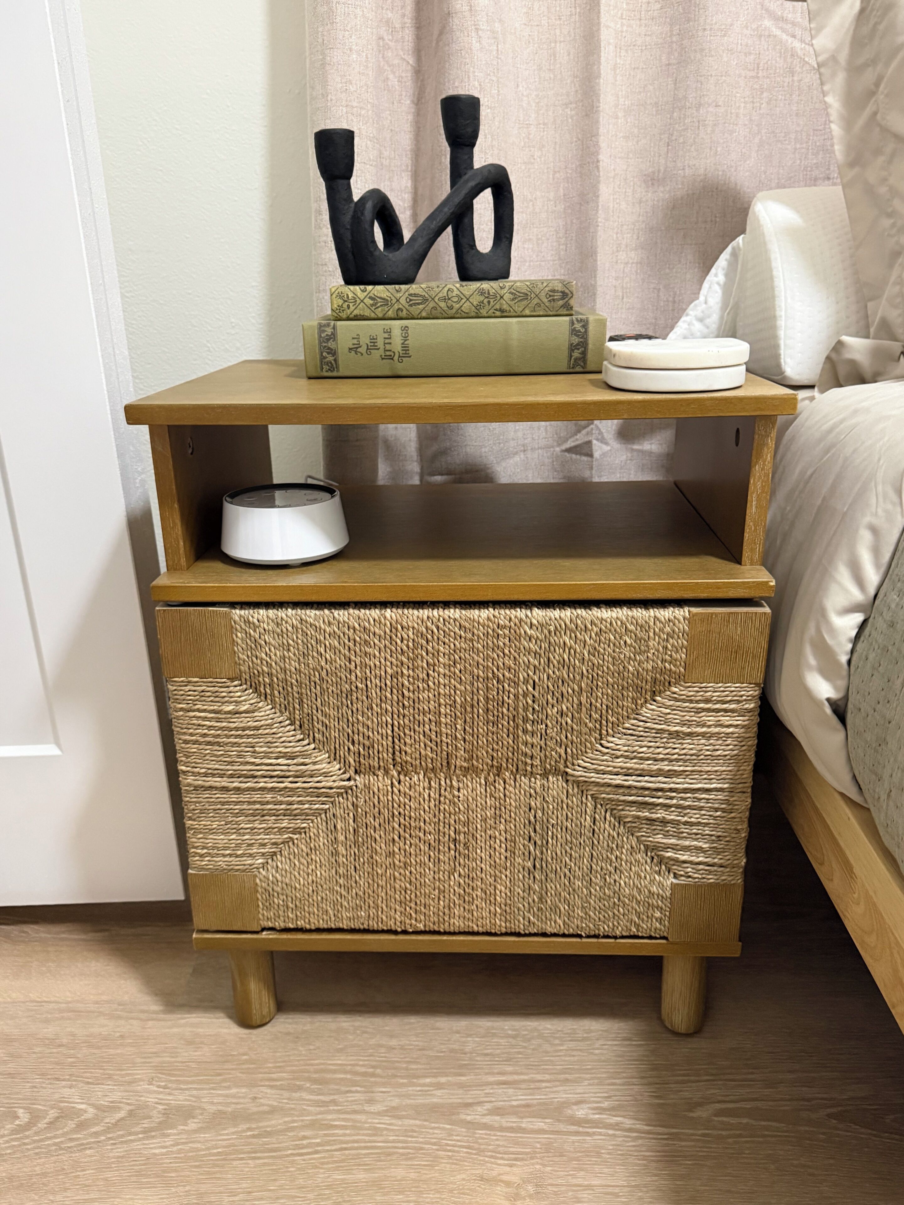 A wooden nightstand with a woven basket and a book titled 'All the Little Things.'