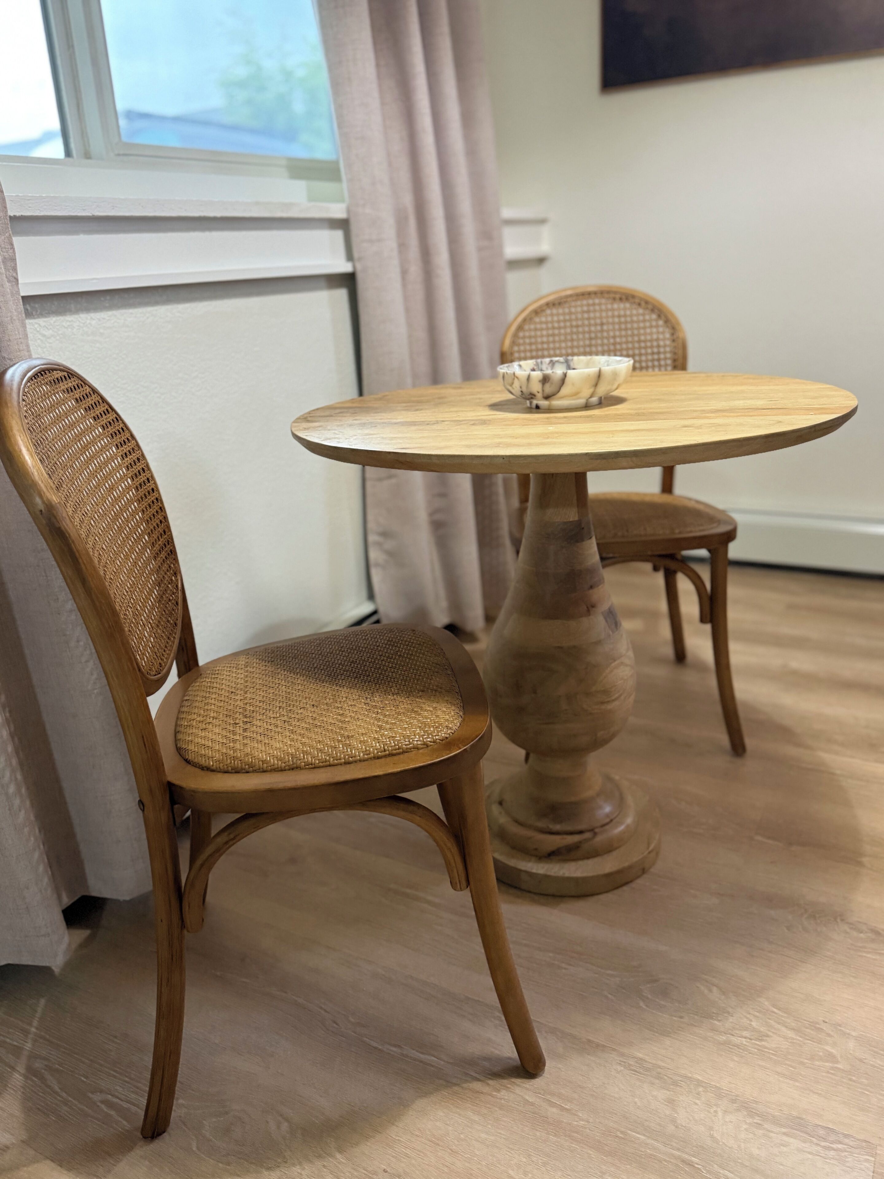 Un coin repas avec une table ronde en bois et deux chaises en osier.