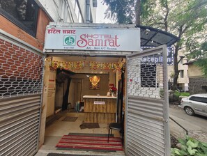 A hotel entrance with a reception desk, a signboard, and a small shrine. - Hotel Samrat (Nashik)