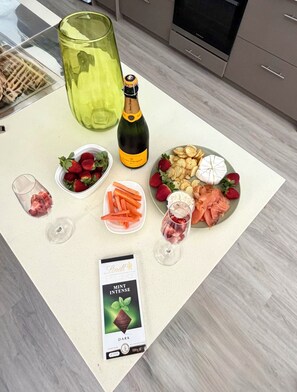 Ein Tisch mit einer Champagnerflasche, Erdbeeren, Karotten, Käse, Crackern und einer Schachtel dunkle Minzschokolade.