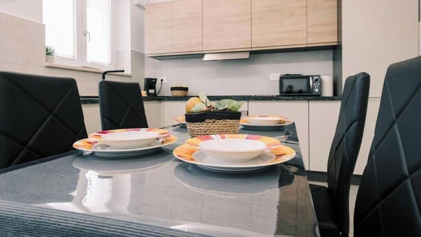 A modern kitchen with a dining table set for four, featuring black chairs and a glass-top table. - Daisy Apartment – Modern Comfort with a Balcony in Molfetta (Molfetta)