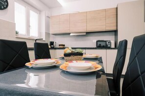 A modern kitchen with a dining table set for four, featuring black chairs and a glass-top table. - Daisy Apartment – Modern Comfort with a Balcony in Molfetta (Molfetta)