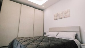 A bedroom with a bed, a nightstand, a wall-mounted artwork, and a sliding door. - Daisy Apartment – Modern Comfort with a Balcony in Molfetta (Molfetta)