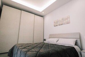 A bedroom with a bed, a nightstand, a wall-mounted artwork, and a sliding door. - Daisy Apartment – Modern Comfort with a Balcony in Molfetta (Molfetta)