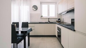 A modern kitchen with a dining area, featuring a clock, a window, and a stove. - Daisy Apartment – Modern Comfort with a Balcony in Molfetta (Molfetta)