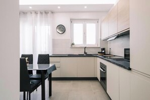 A modern kitchen with a dining area, featuring a clock, a window, and a stove. - Daisy Apartment – Modern Comfort with a Balcony in Molfetta (Molfetta)