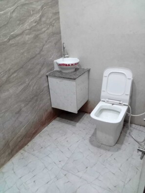 A bathroom with a toilet, a sink, and a marble wall. - Hotel Emerald Inn (Patna)
