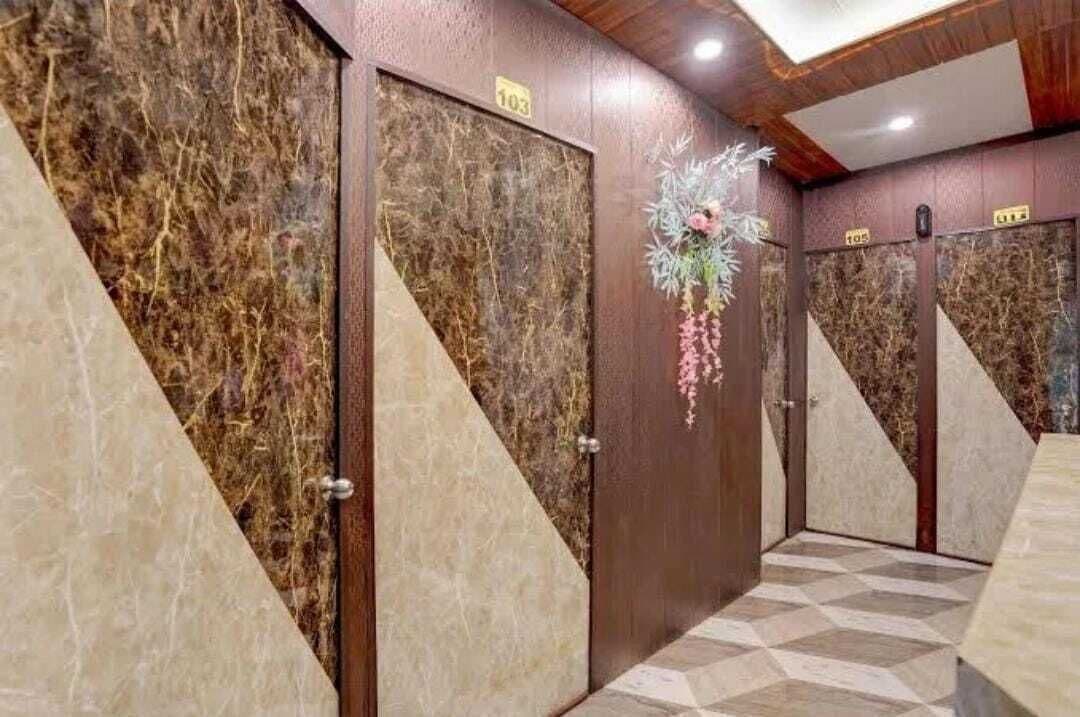 Pasillo de hotel con paredes de mármol, puertas numeradas y un piso con estampado geométrico.