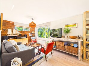 A cozy living room with a sofa, a red chair, a coffee table, a TV, and a bookshelf.
