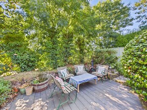 An outdoor deck with a wooden table and two chairs, surrounded by lush greenery and trees.
