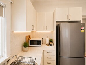 A modern kitchen with white cabinets, a stainless steel refrigerator, a microwave, and a small countertop with a plant and kitchen items.