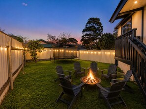 A backyard with a fire pit surrounded by chairs, a trampoline, and string lights along the fence.