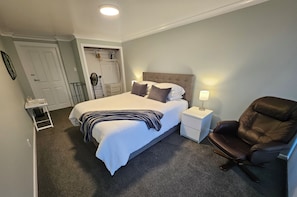 A neatly arranged bedroom with a bed, bedside table, lamp, and a leather chair.