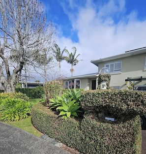 A residential area with a well-maintained garden, a hedge with a sign, and a building with a number sign.