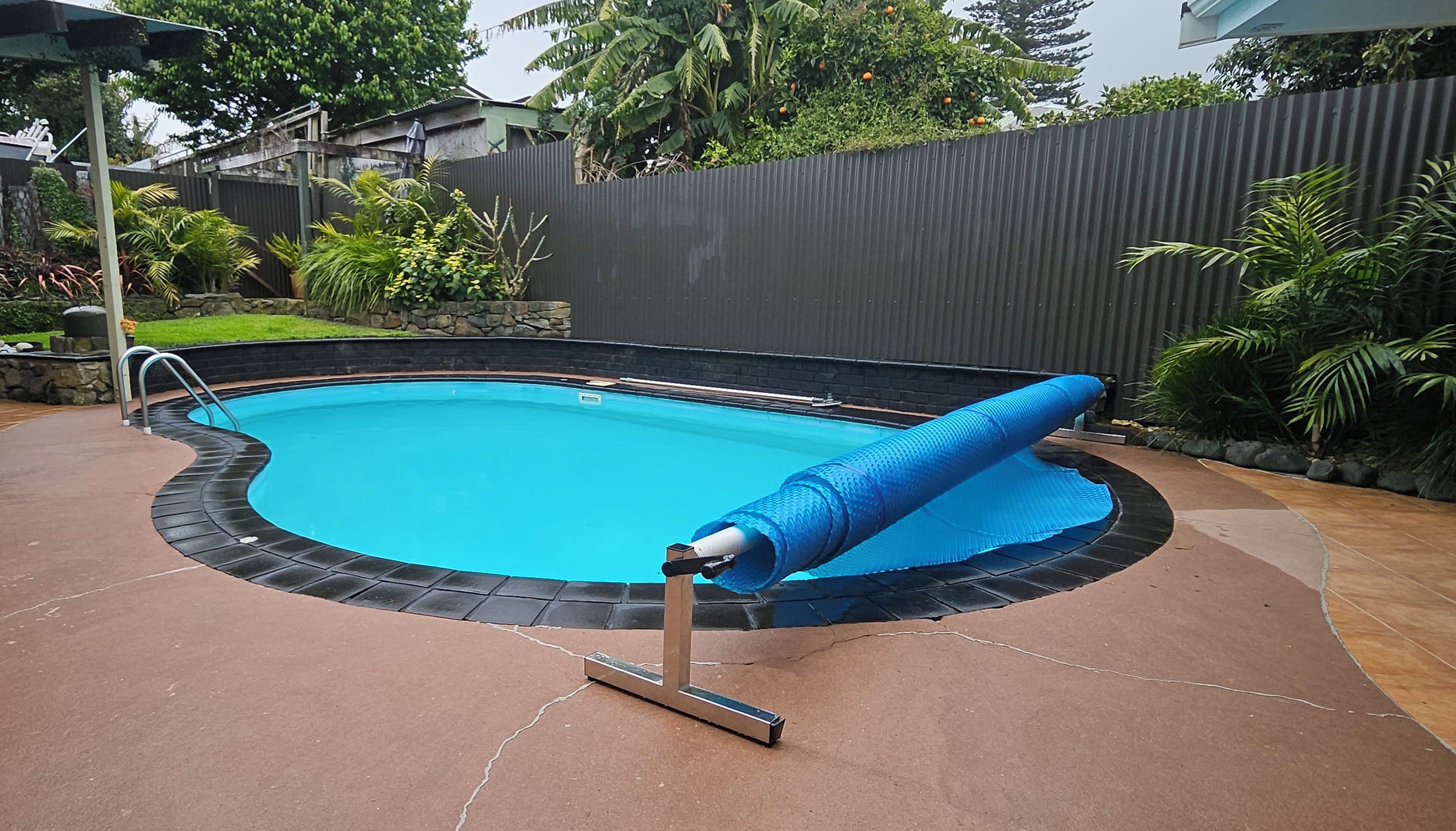 A swimming pool with a blue cover, surrounded by a brick deck and a stone wall.