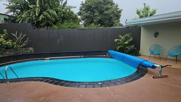 Una piscina con una cubierta azul, una escalera y un borde con baldosas.