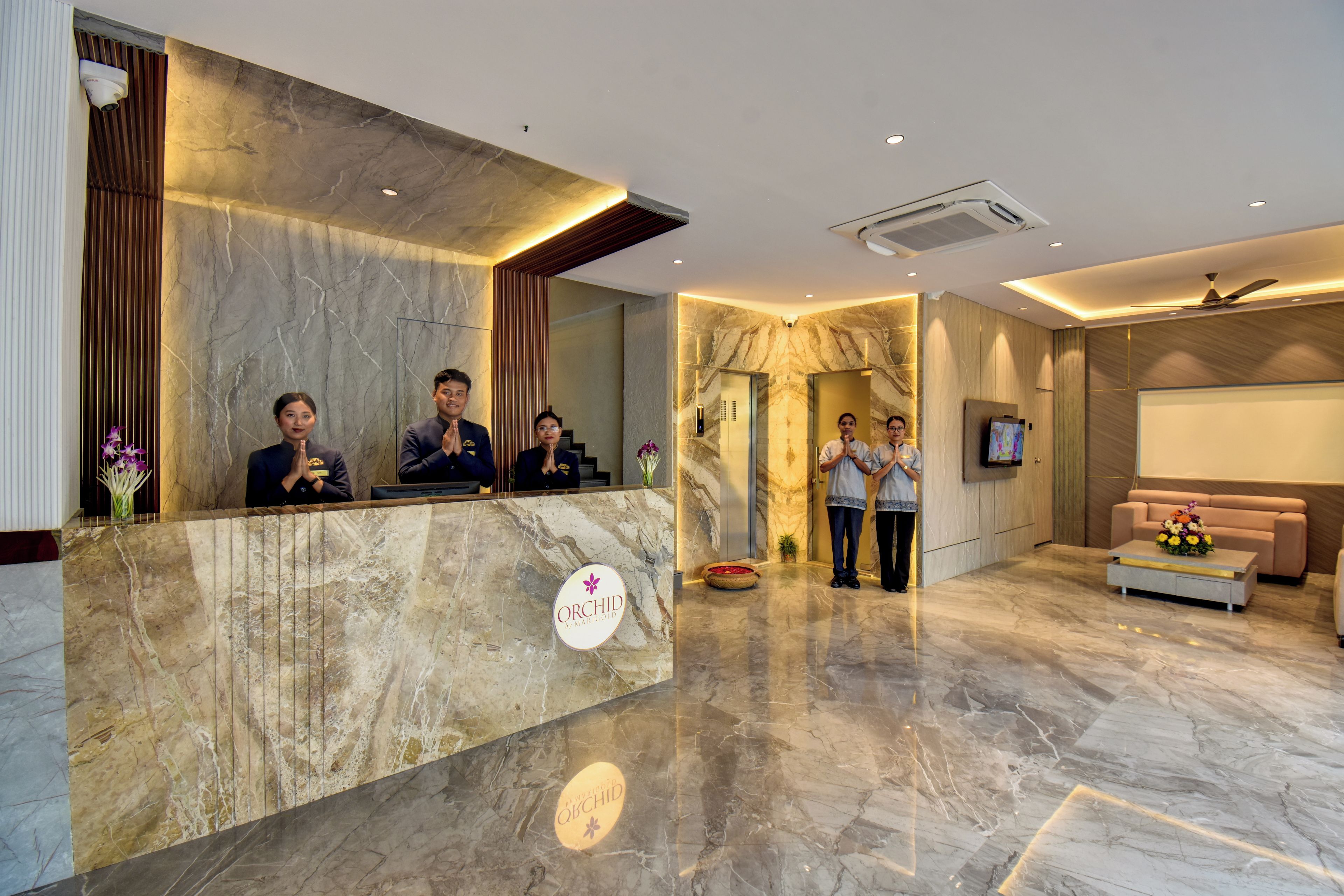 Zona de recepción de un hotel con suelo de mármol, un mostrador de recepción, un sofá y una pantalla de televisión.