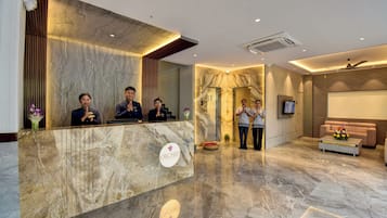 Zona de recepción de un hotel con suelo de mármol, un mostrador de recepción, un sofá y una pantalla de televisión.