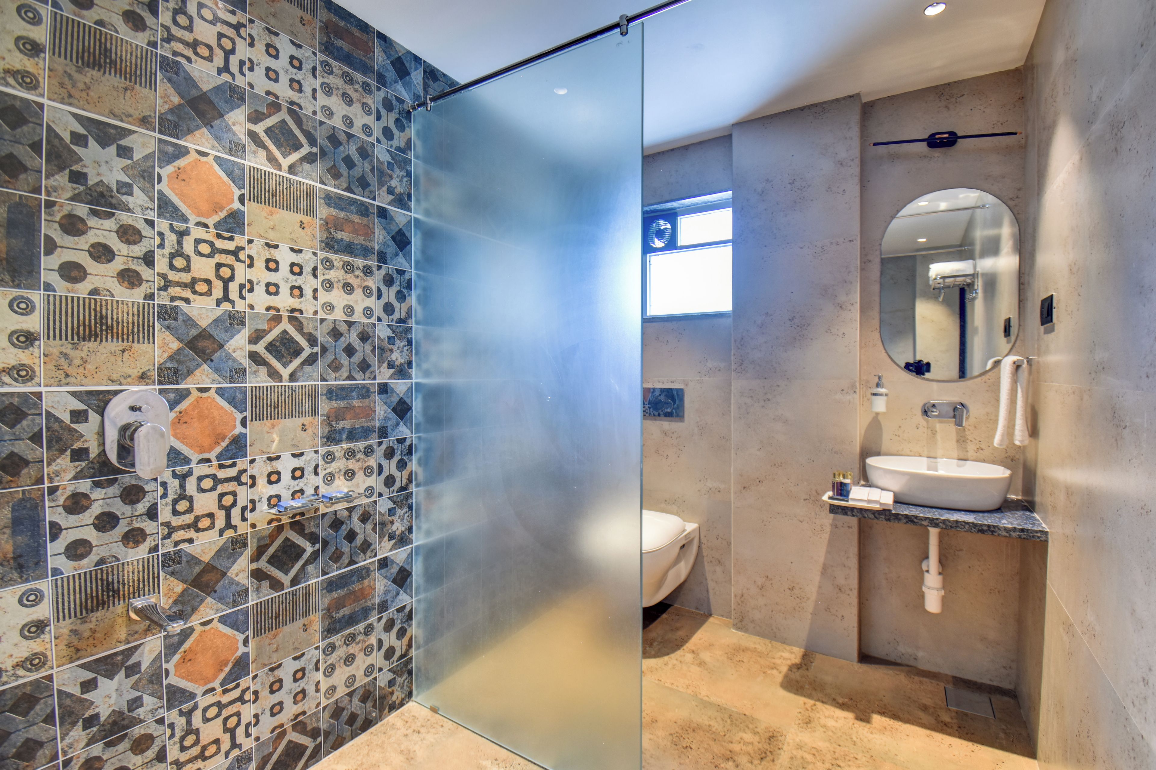 A modern bathroom with patterned tiles, a glass partition, a toilet, a sink, and a mirror.