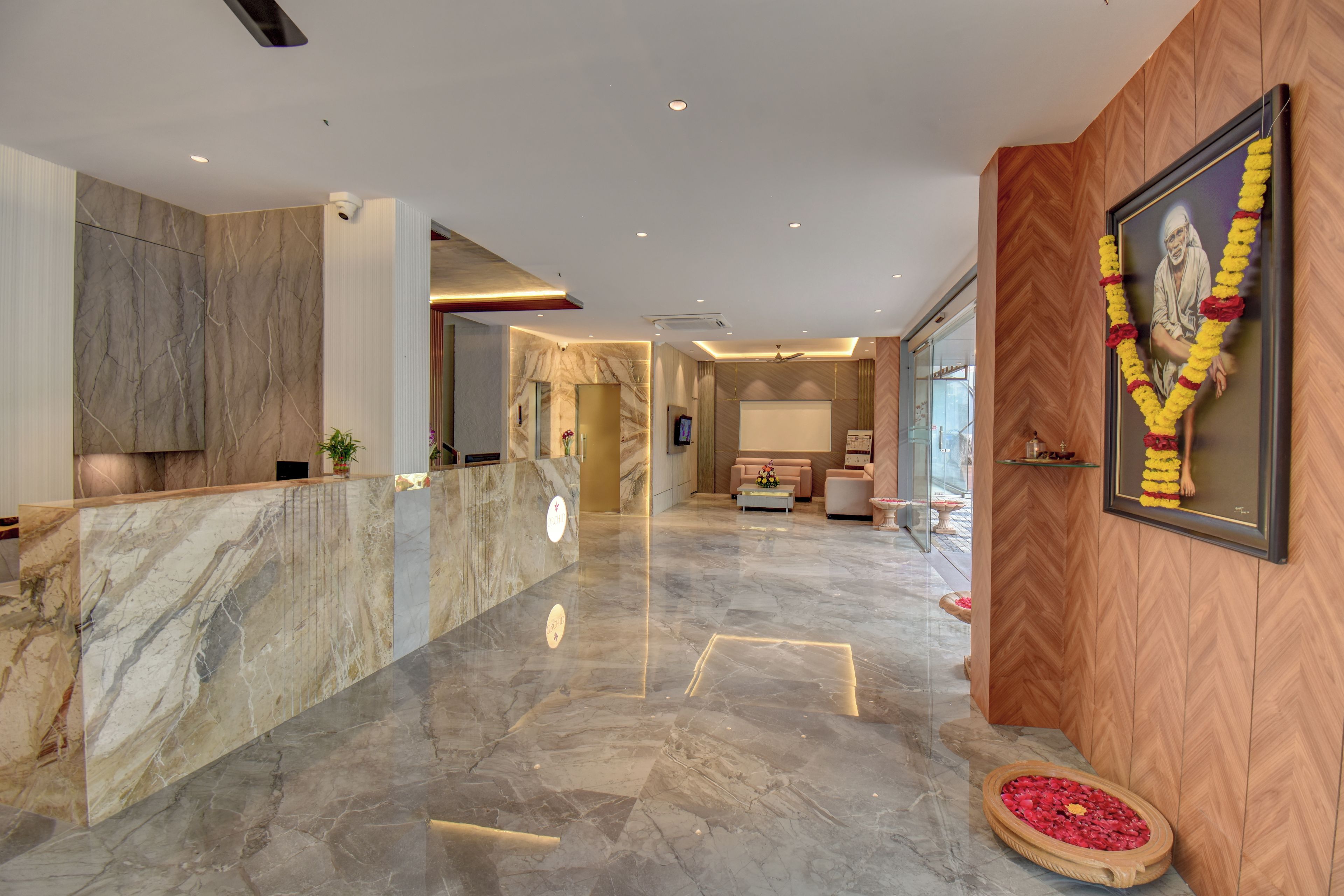 A hotel lobby with marble flooring, a reception desk, a seating area with a sofa, and a framed portrait on the wall.