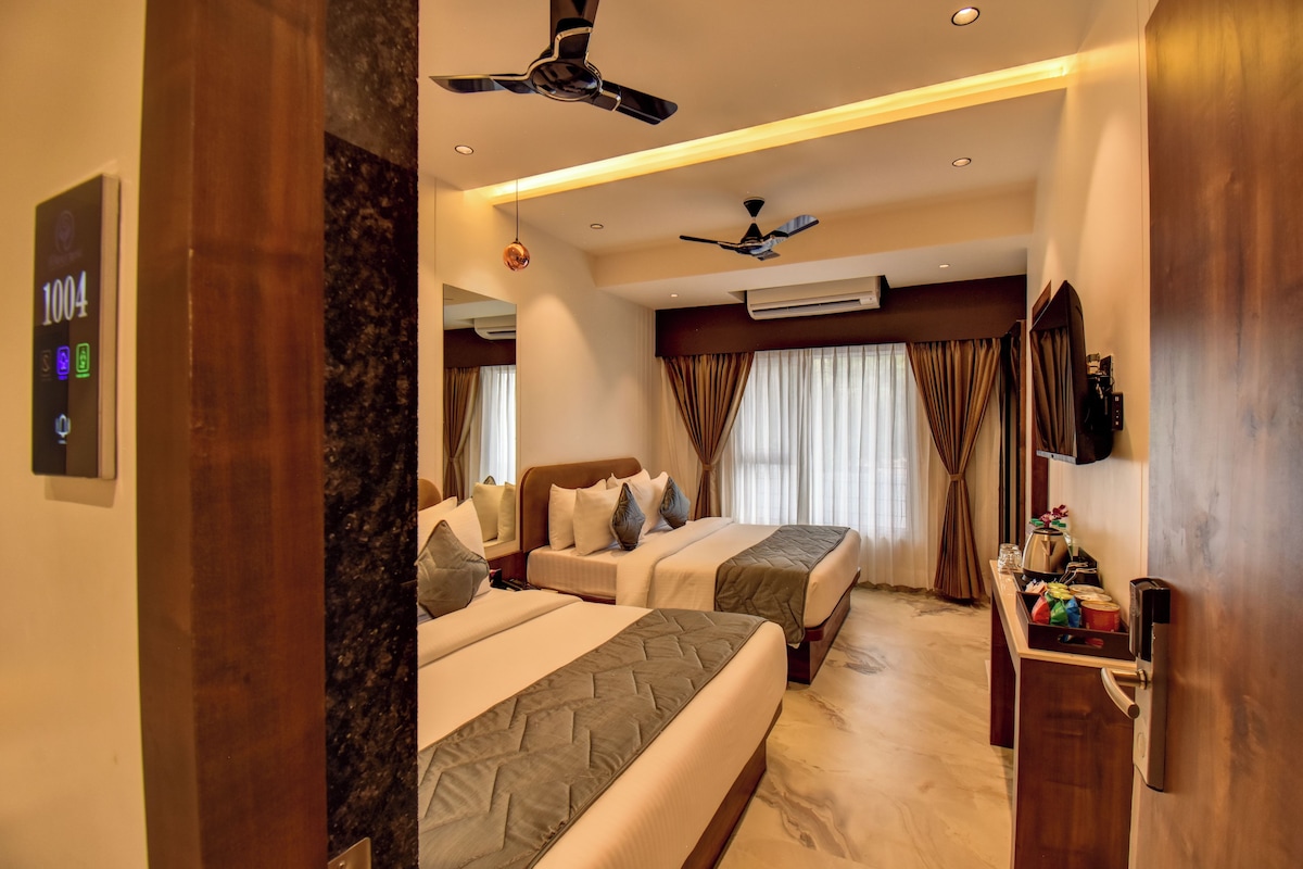Une chambre d’hôtel avec deux lits, un ventilateur de plafond, un appareil de climatisation, un mini-bar et un grand miroir.