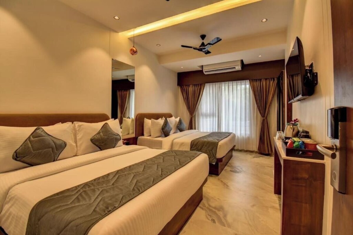 A hotel room with two beds, a TV, a desk, and an air conditioning unit.