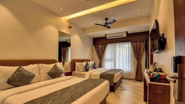 Habitación de hotel con dos camas, televisión, escritorio y aire acondicionado.