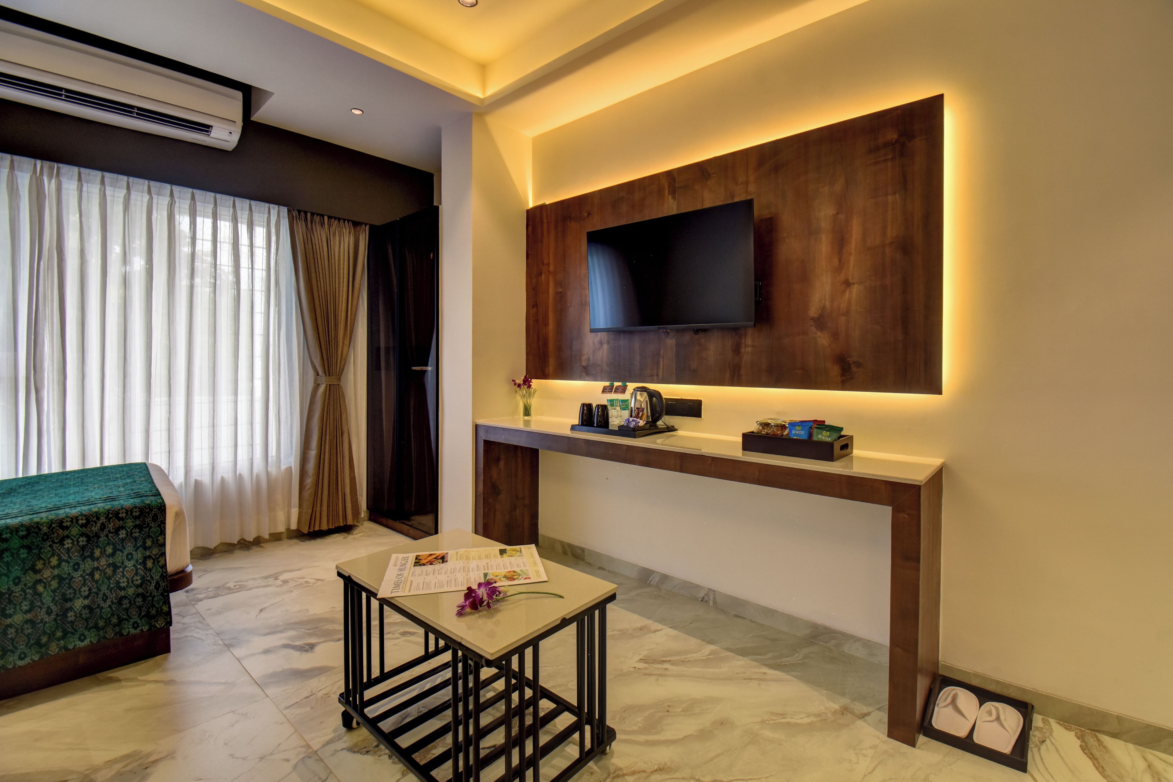 Una habitación de hotel moderna con un televisor de pantalla plana montado en un panel de madera, una mesita con un menú y una cama con cubrecama verde.
