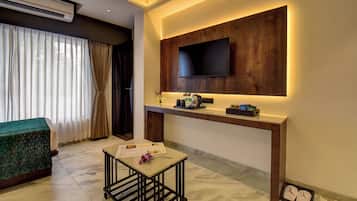 Una habitación de hotel moderna con un televisor de pantalla plana montado en un panel de madera, una mesita con un menú y una cama con cubrecama verde.