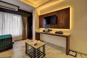 Une chambre d’hôtel moderne dotée d’un téléviseur à écran plat fixé sur un panneau en bois, d’une petite table avec un menu et d’un lit recouvert d’une couverture verte.