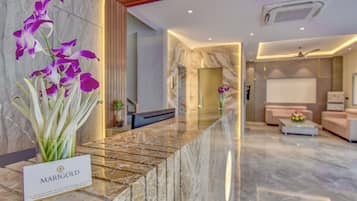 A reception area with a marble counter, a sign reading 'MARG GOLD', and a view into a living area with a sofa and a coffee table.