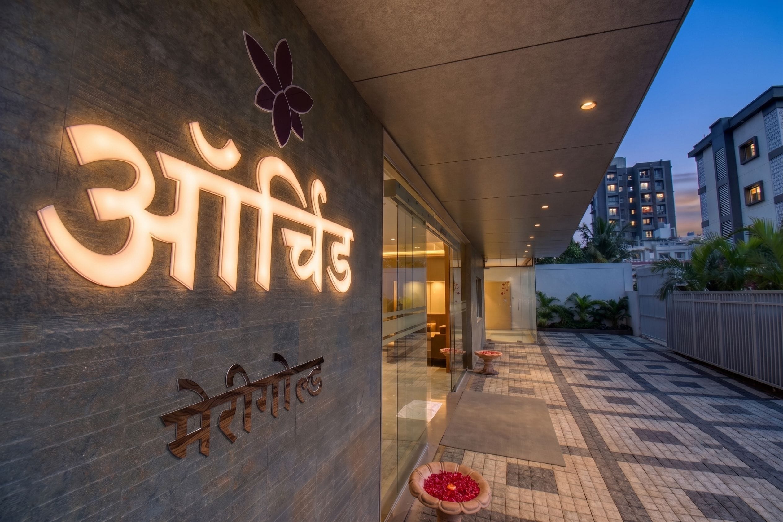 A hotel entrance with a sign in Hindi and English, a covered walkway, and a tiled patio area.