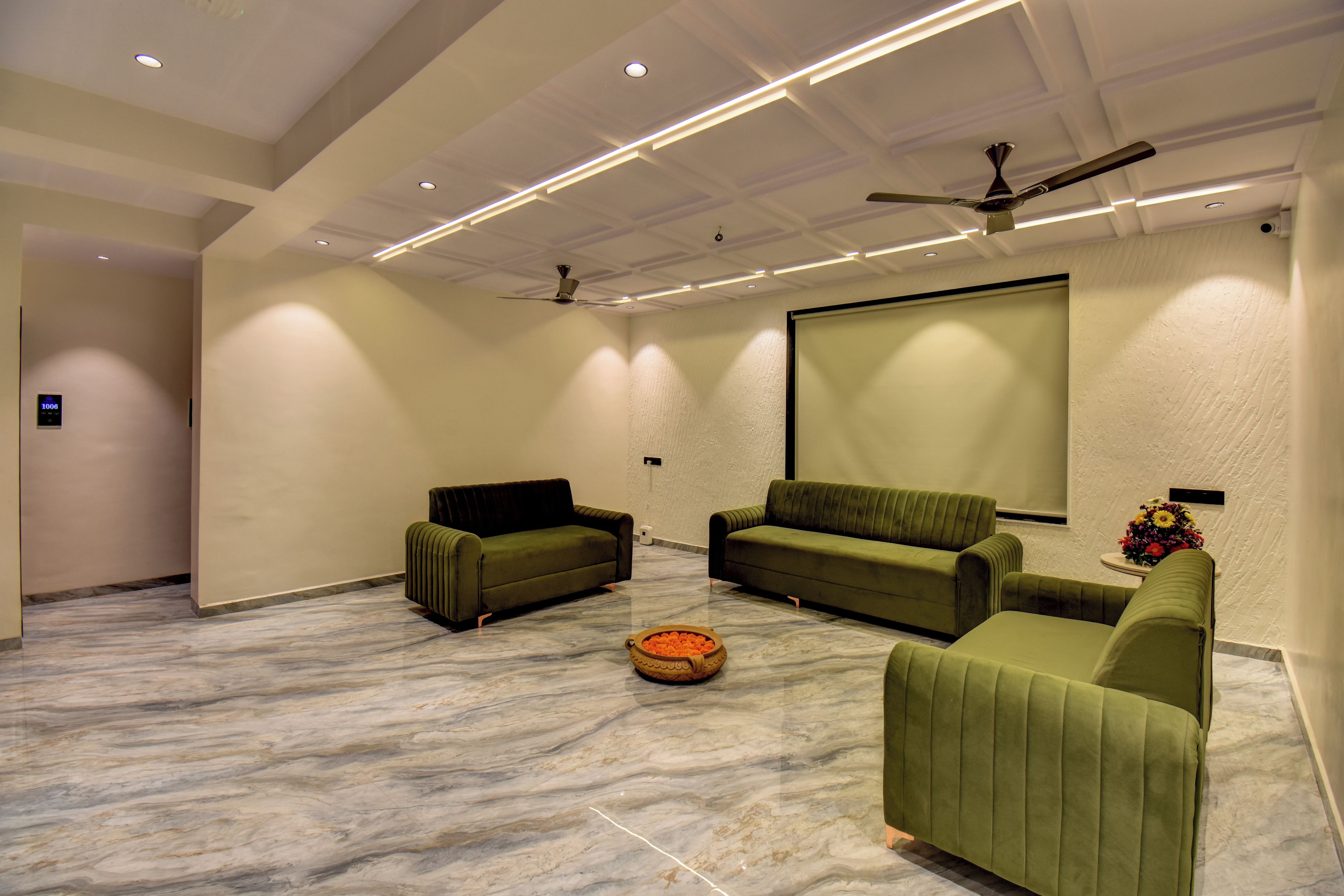 A spacious room with a large screen, two sofas, a ceiling fan, and a marble floor.