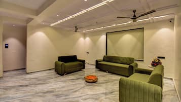 A spacious room with a large screen, two sofas, a ceiling fan, and a marble floor.