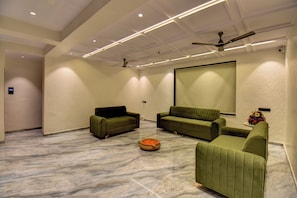 A spacious room with a large screen, two sofas, a ceiling fan, and a marble floor. - Hotel Orchid by Marigold, Shirdi - Premium Comfort Near Sai Baba Temple (Rahata)