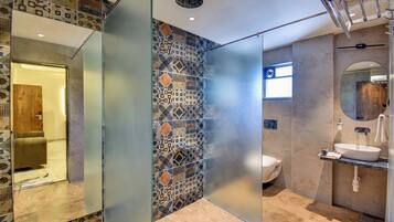 Een moderne badkamer met een glazen douchewand, decoratieve tegels, een toilet en een wastafel met spiegel.