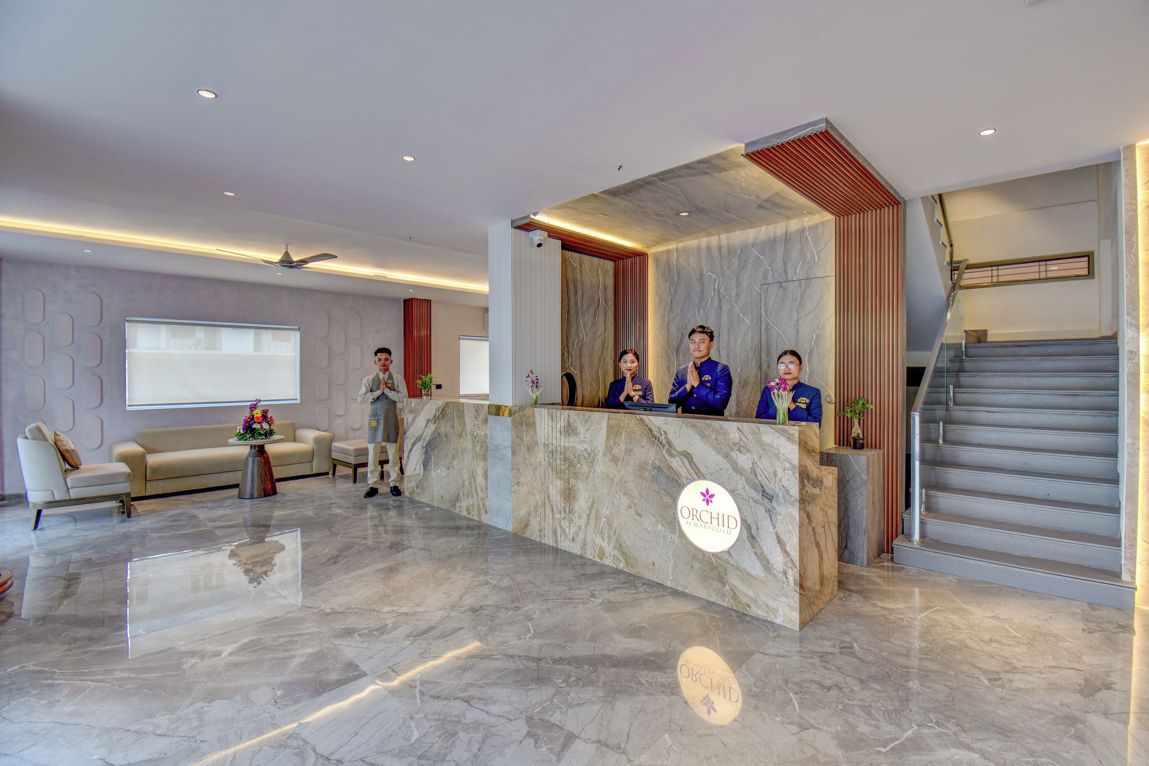 A hotel reception area with a marble reception desk, a sofa, and a staircase.