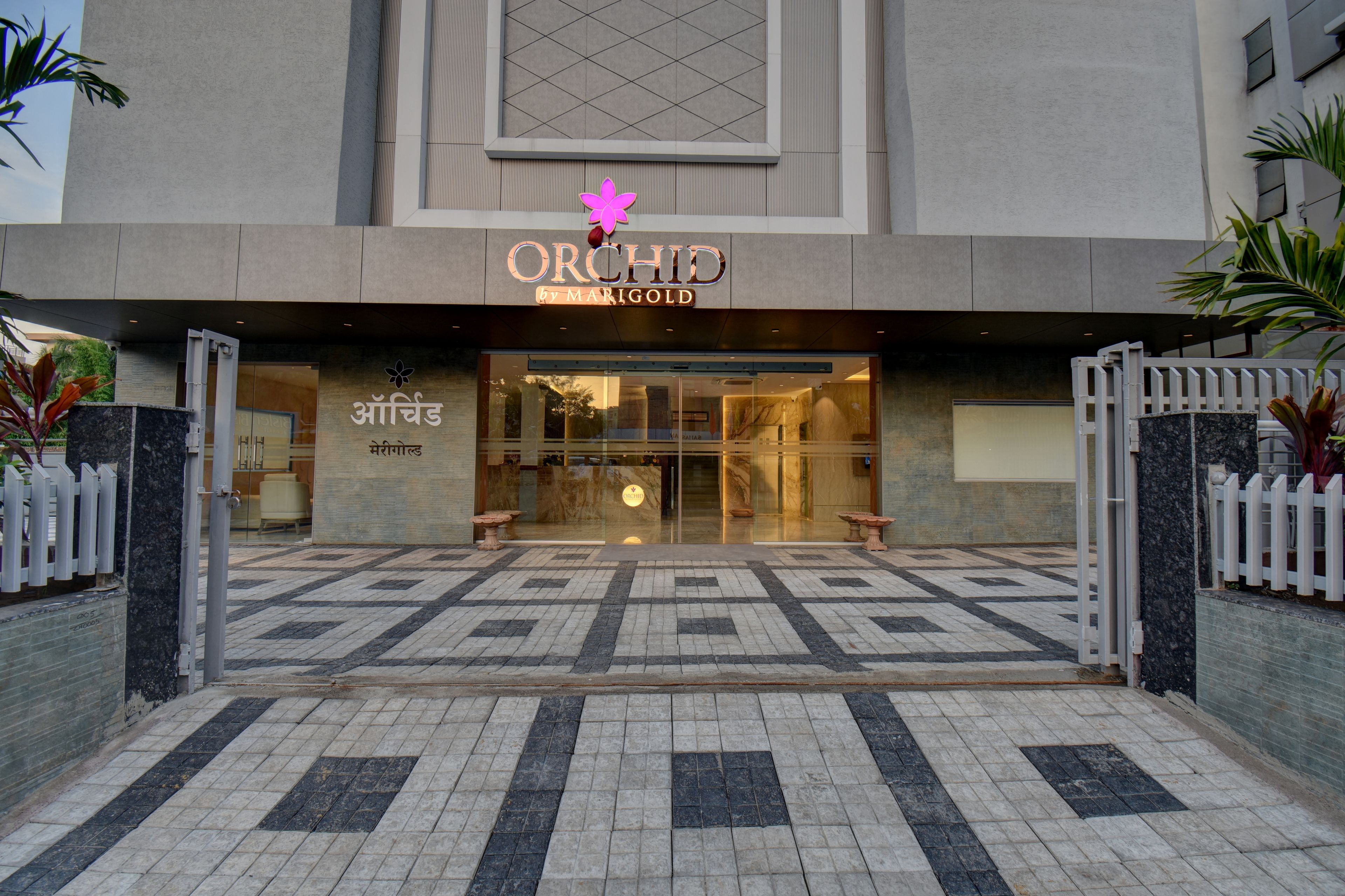 The entrance to a hotel with a modern design, featuring a large glass facade and a decorative flower emblem above the entrance.