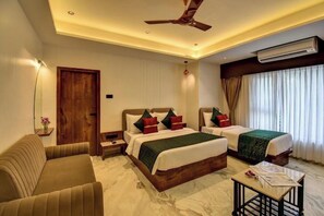 A hotel room with two beds, a sofa, a small table, an air conditioning unit, and a ceiling fan. - Hotel Orchid by Marigold, Shirdi - Premium Comfort Near Sai Baba Temple (SHIRDI MAHARASHTRA)