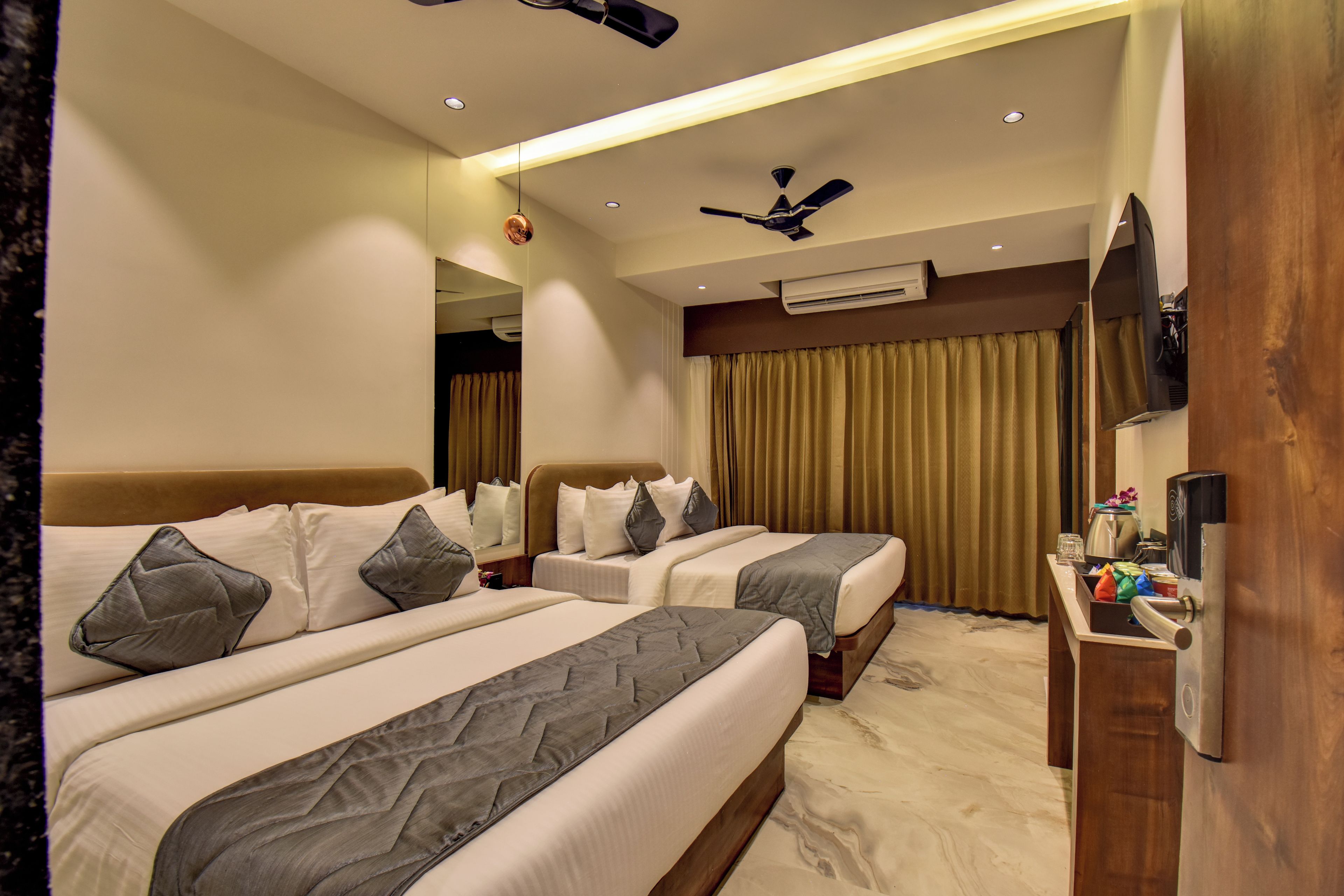 Habitación de hotel con dos camas, televisión, aire acondicionado y ventilador de techo.