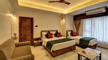 A hotel room with two beds, a sofa, a small table, an air conditioning unit, and a ceiling fan.