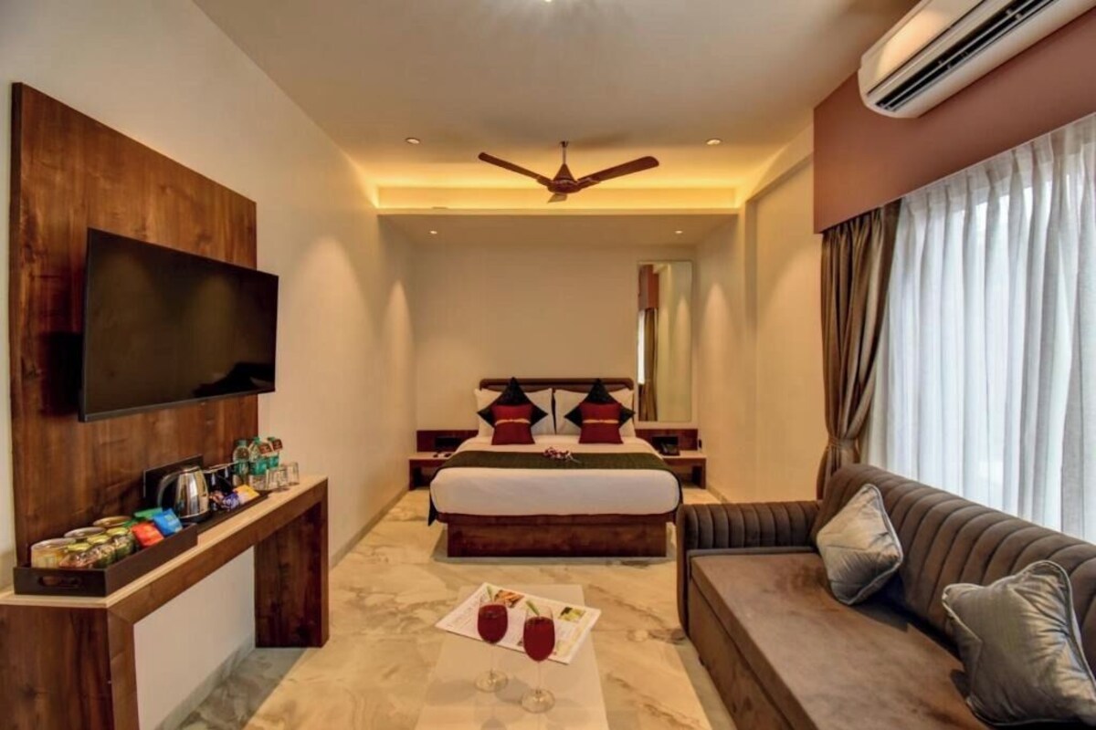 A hotel room with a bed, a sofa, a TV, a ceiling fan, and an air conditioning unit.