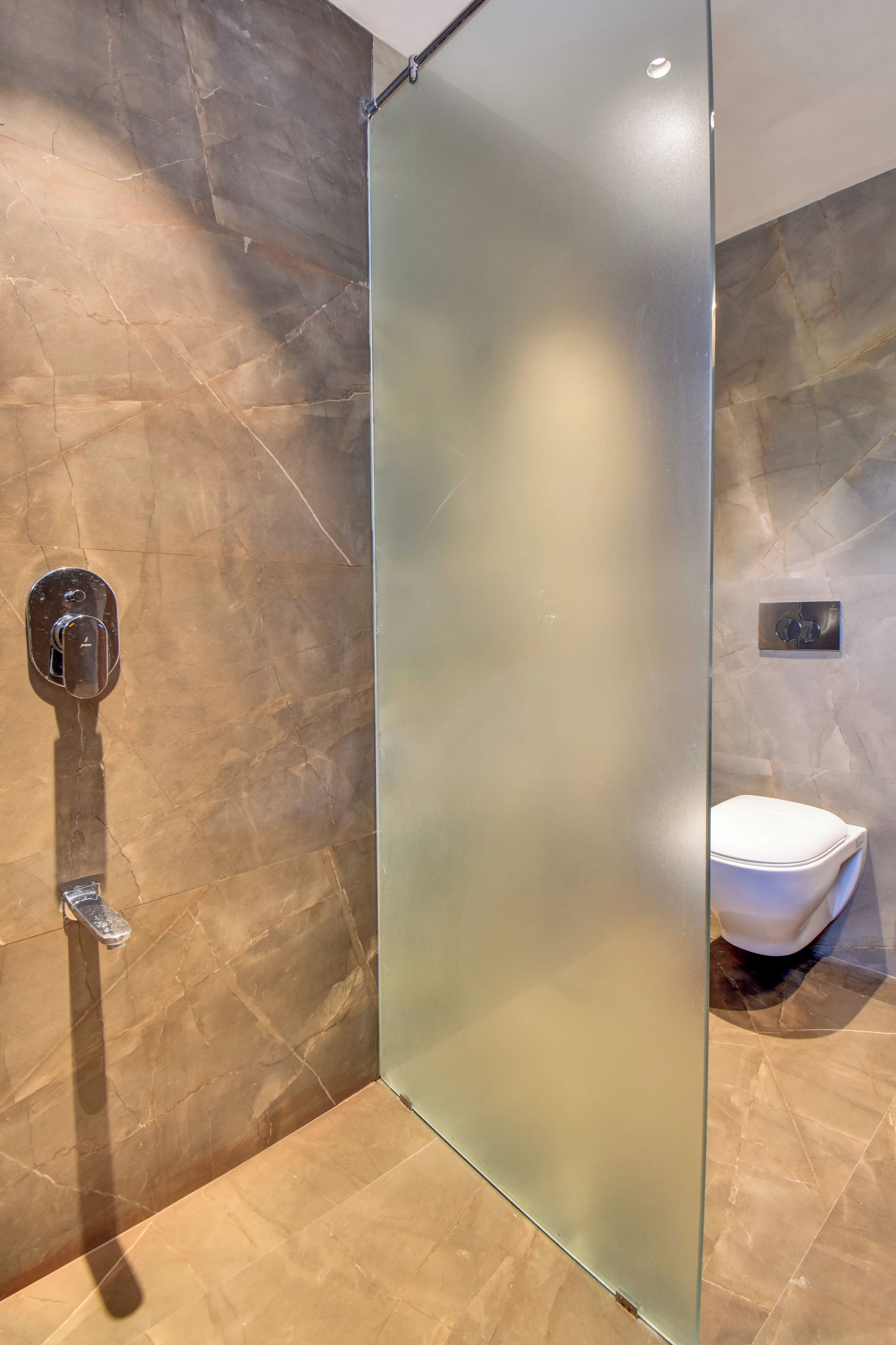 A modern bathroom with a glass shower enclosure, a toilet, and a wall-mounted faucet.