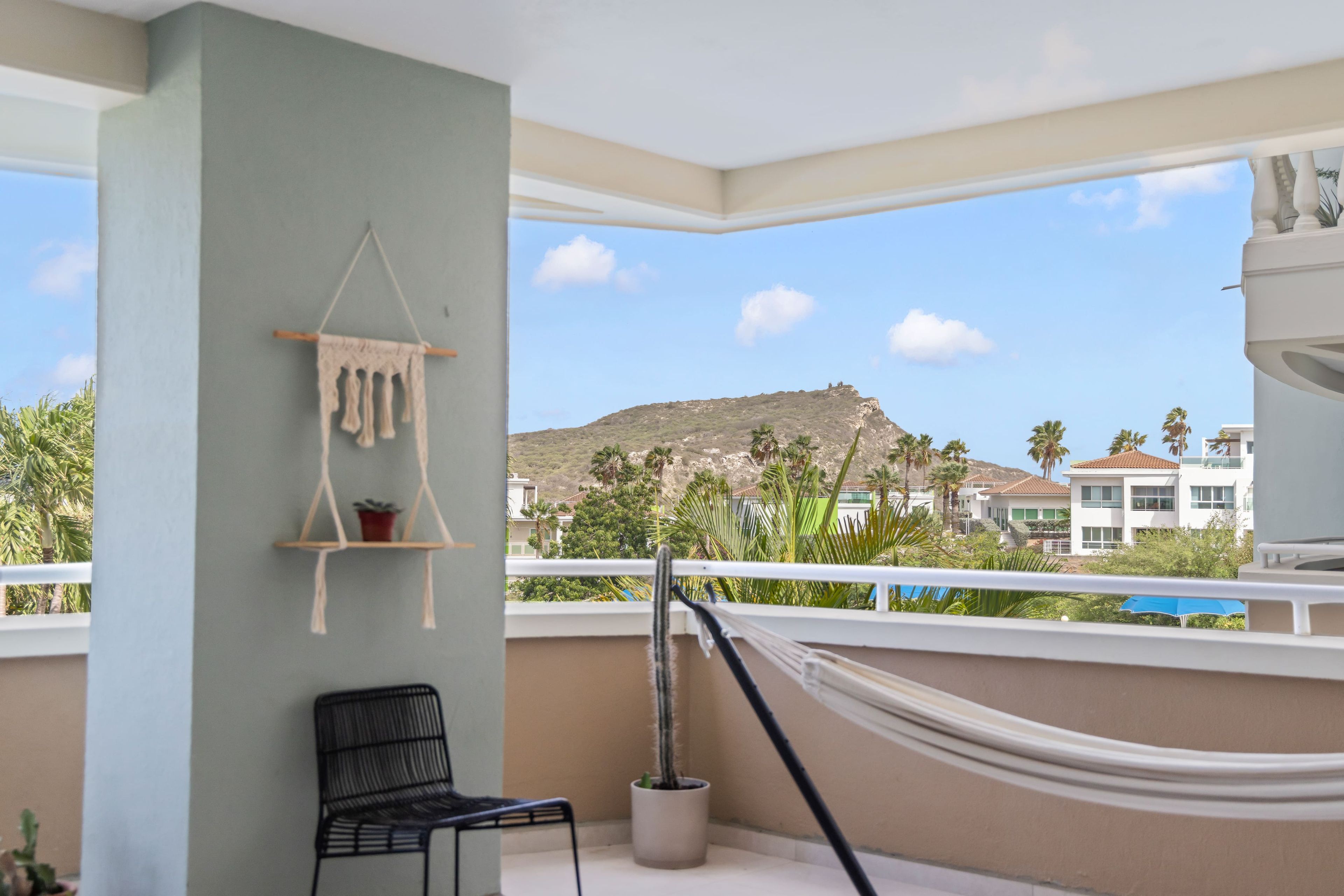 A balcony with a hammock, a chair, and a macrame wall hanging.