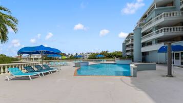 A pool area with lounge chairs and umbrellas, surrounded by a building with balconies.