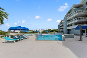 A pool area with lounge chairs and umbrellas, surrounded by a building with balconies. - Ocean view apartment near Piscadera beach (Curacao)