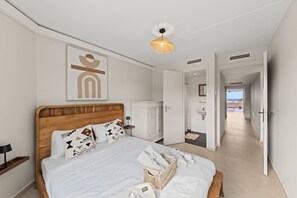 Una camera d'albergo con un letto in legno, un comodino, una lampada, un'opera d'arte appesa al muro, un lampadario e vista mare attraverso una porta aperta.