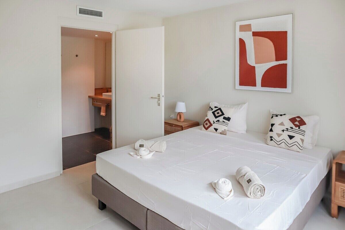 A hotel room with a bed, a nightstand, a wall-mounted artwork, and a door leading to a bathroom.