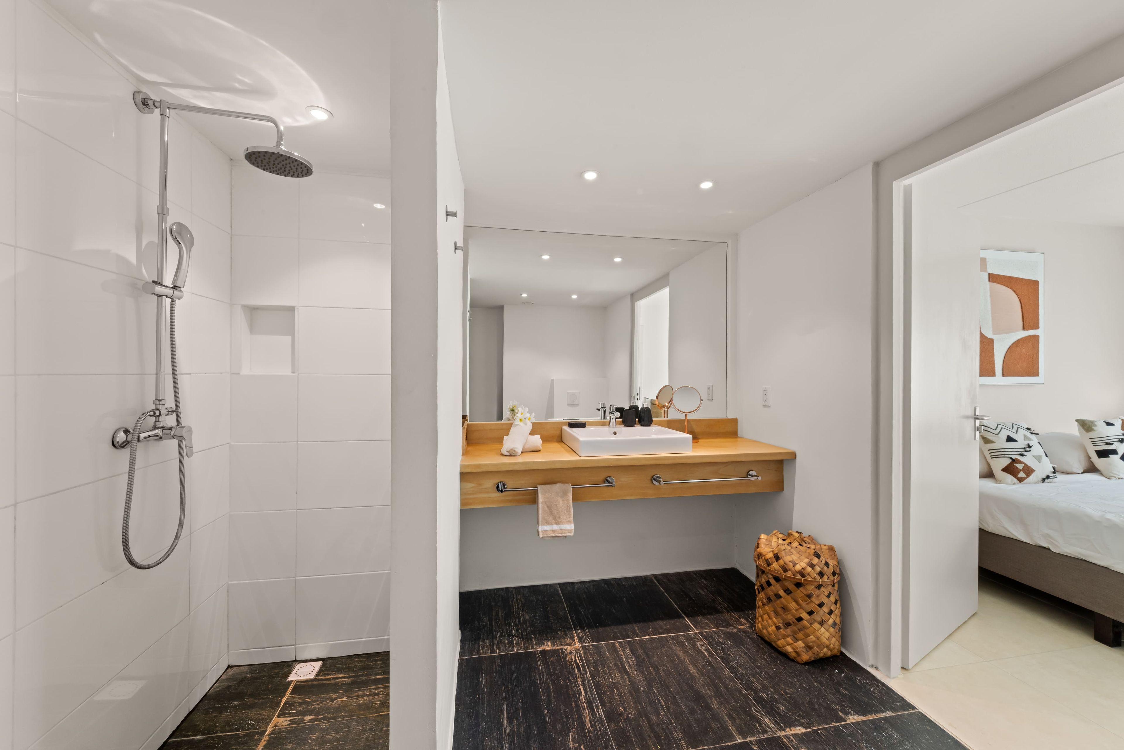 Une salle de bain moderne avec une douche, un meuble-lavabo en bois et un lit avec des oreillers.