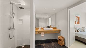 Une salle de bain moderne avec une douche, un meuble-lavabo en bois et un lit avec des oreillers.